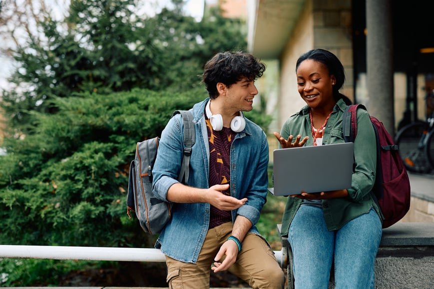 two college students on campus looking at laptop